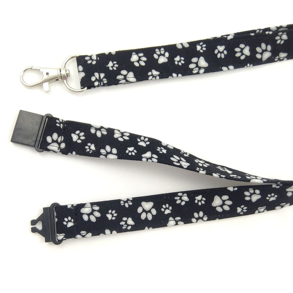 Close up of black fabric lanyard with white paw prints showing metal swivel clasp and black plastic safety buckle